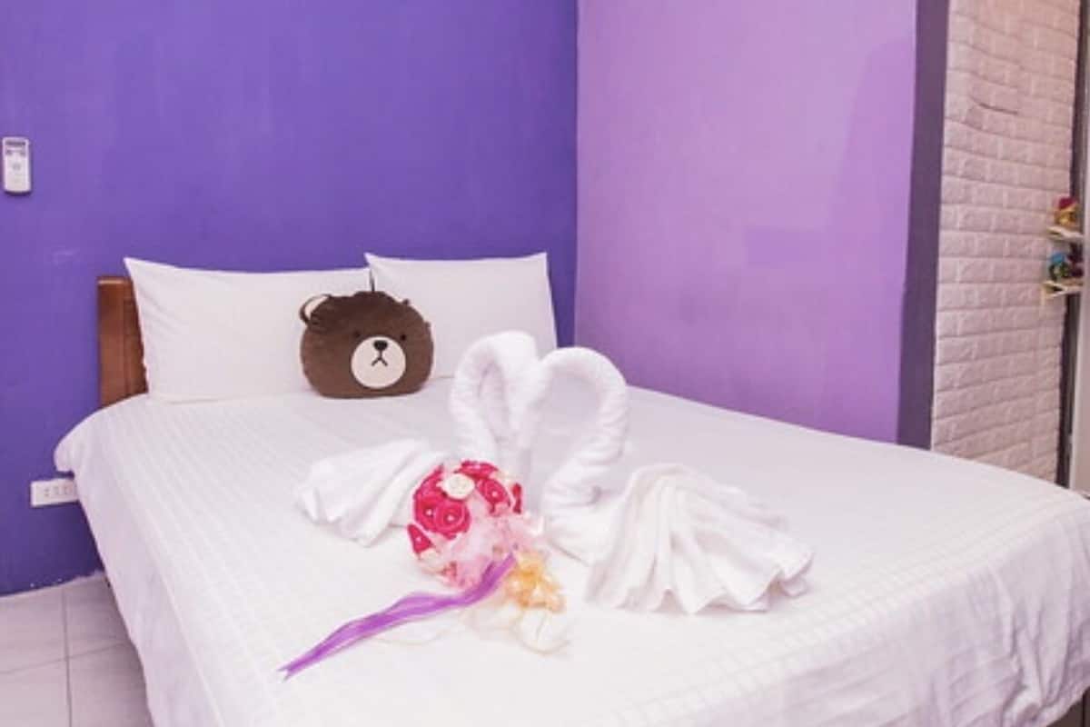 A hotel room with a bed, a bear-shaped pillow, and a towel with a heart-shaped design.