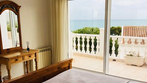 A bedroom with a large bed, a wooden dresser, a mirror, and a view of the sea through a balcony. - Stunning Detached 3 Bedroom Villa with Private Pool and Sea View  (Peñíscola)