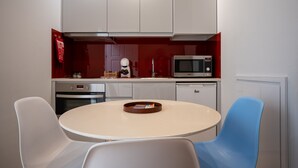 Una cocina moderna con armarios blancos, un microondas, un horno y un lavavajillas. Hay una mesa redonda con dos sillas, una blanca y otra azul.