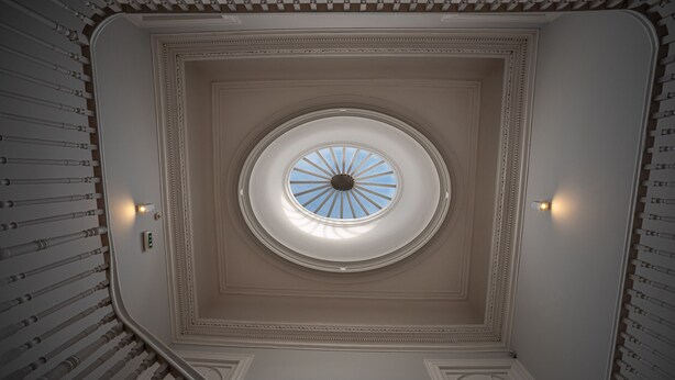 Un tragaluz grande y circular con diseño radial, rodeado de molduras ornamentales y una escalera simétrica.