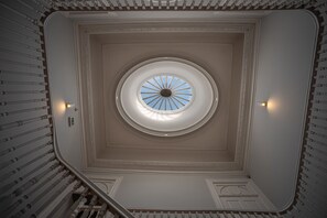 Ett storslaget, runt takfönster med ett utåtriktat mönster, omgivet av utsmyckade lister och en symmetrisk trappa.