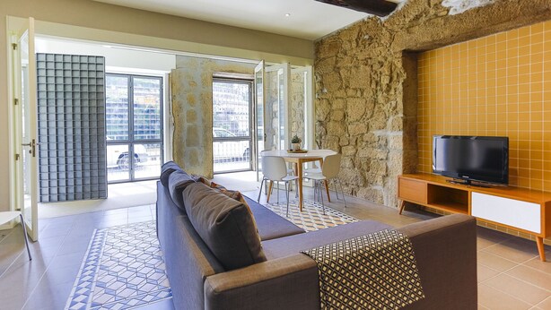 Un salon moderne avec un canapé, une table à manger et des chaises, un téléviseur et un mur en pierre.