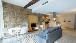 Un salon moderne avec un mur en pierre, un canapé gris, une table à manger avec des chaises, un téléviseur et un coin cuisine équipé d’un four à micro-ondes et de placards.