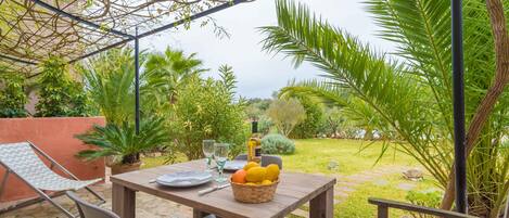 An outdoor patio with a wooden table, chairs, a basket of fruit, and a glass of water.