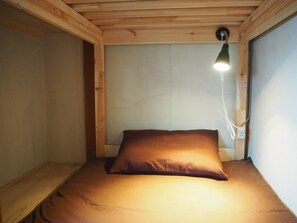 Een kleine kamer met een enkel bed, houten plafond en een bedlampje.