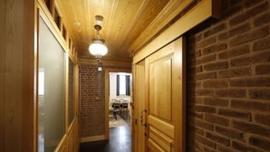 A narrow hallway with wooden walls and a brick wall on one side. There is a door on the right and a window at the end of the hallway.