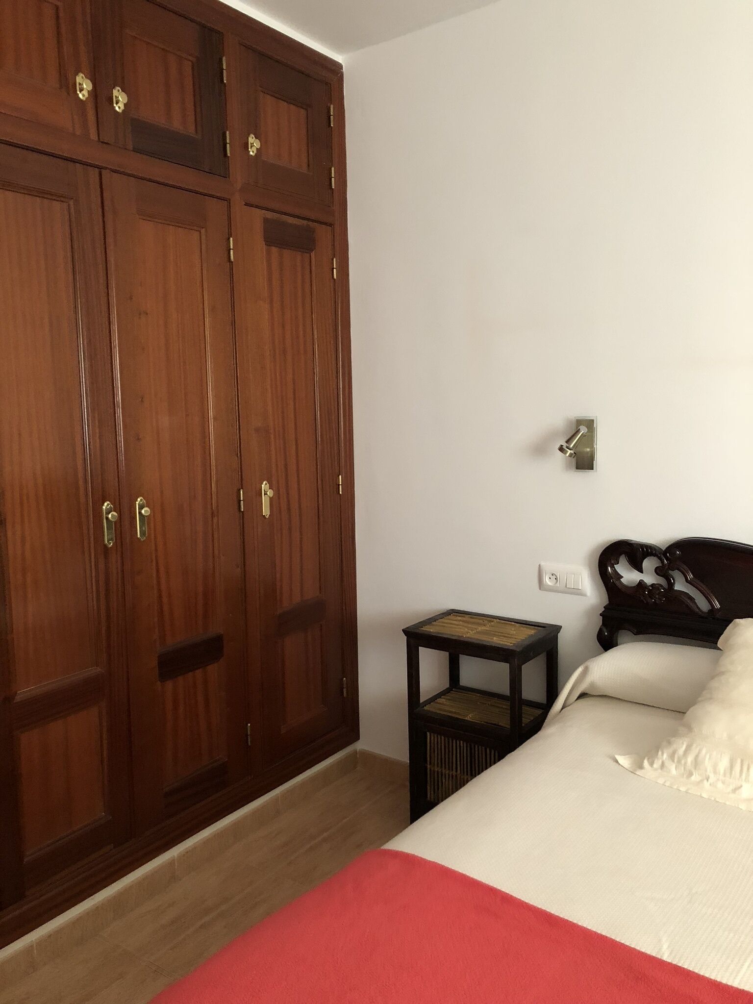 Un dormitorio con cama, un armario de madera, una mesita pequeña y una mesita de noche.