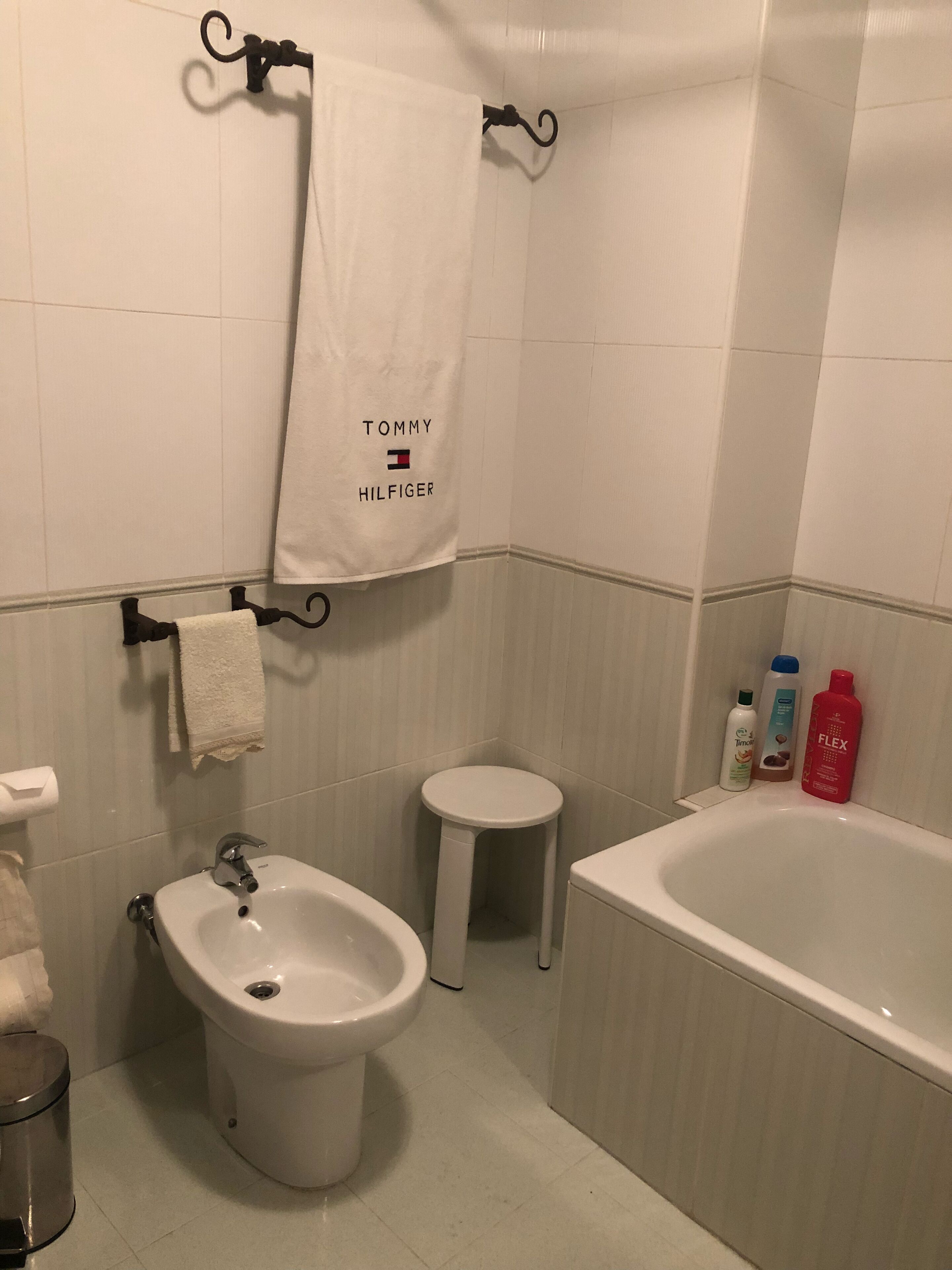 Une salle de bain équipée d’un bidet, de toilettes et d’une baignoire. Des serviettes sont accrochées à des crochets et des articles de toilette sont disposés sur une étagère.