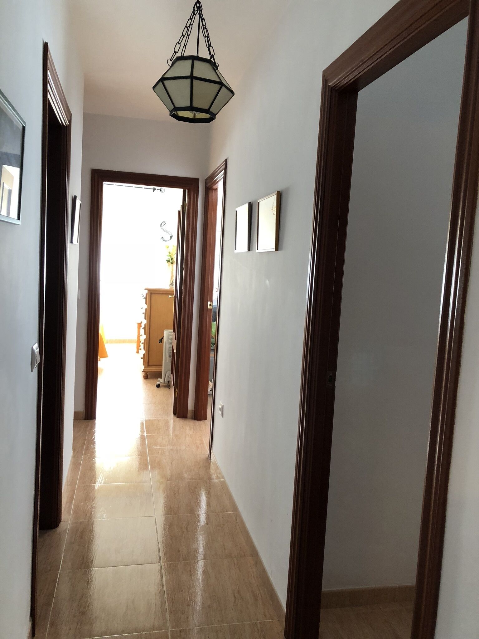 A hallway with a tiled floor, wooden doors, and a hanging light fixture.