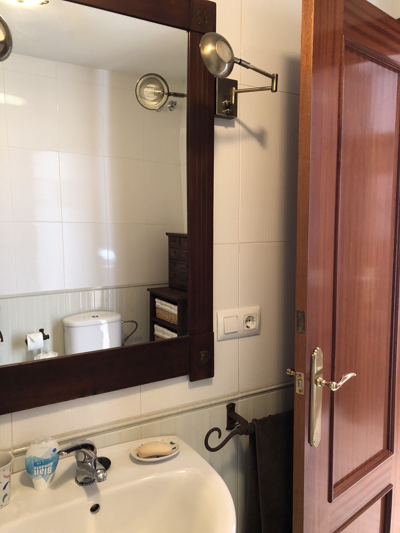 A bathroom with a white sink, a mirror, a towel rack, and a wooden door.