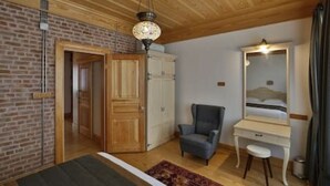 Ein Zimmer mit Holzboden, Ziegelwand, einem Bett, einem Schreibtisch mit Spiegel, einem Stuhl und einem kleinen Teppich.