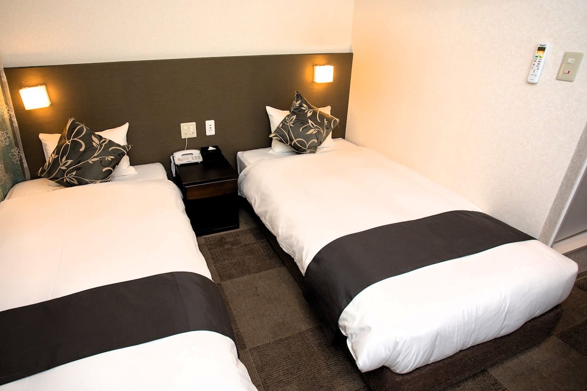 Ein Hotelzimmer mit zwei Betten, einem Nachttisch, einem Telefon und einem an der Wand befestigten Lichtschalter.