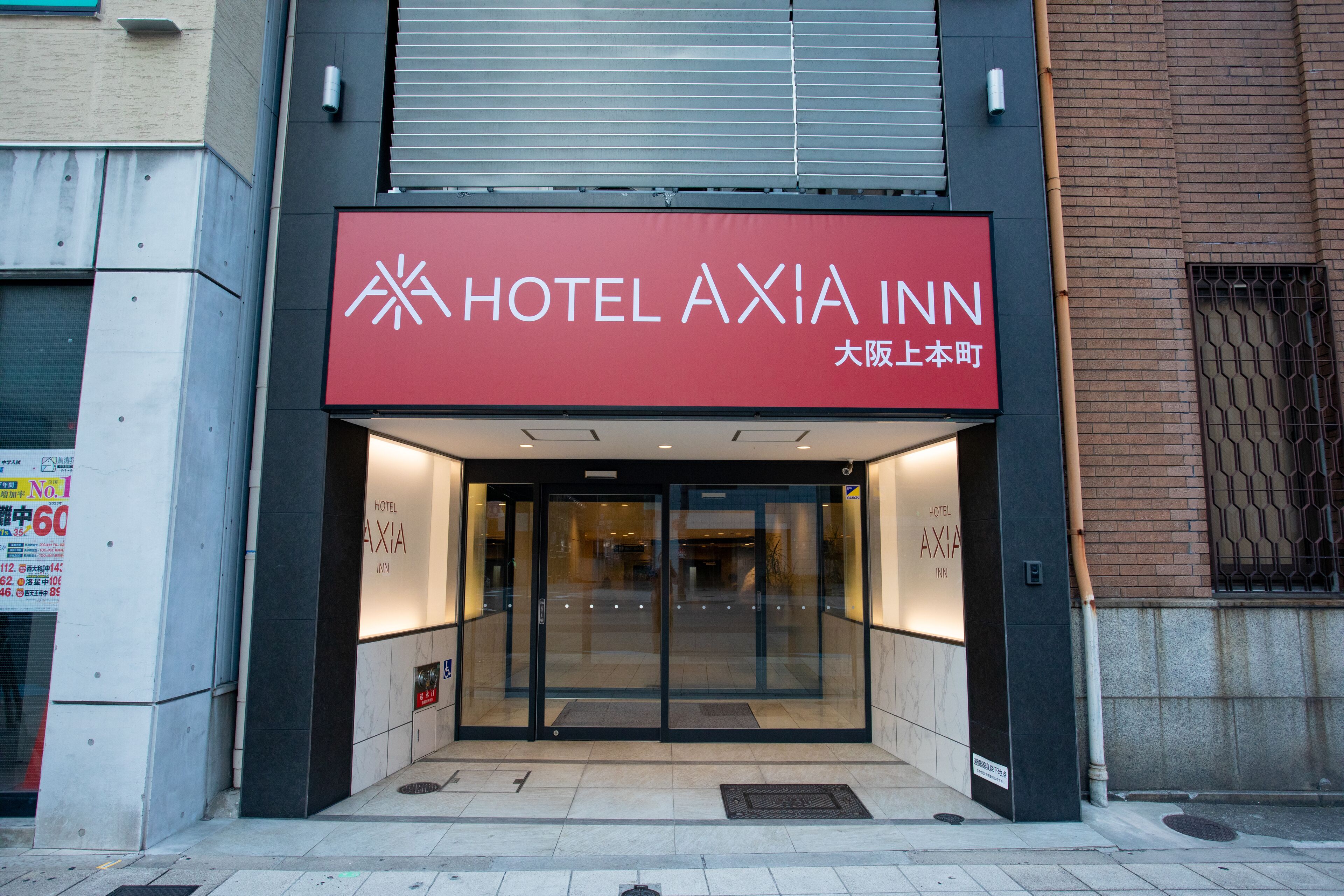 L’entrée de l’hôtel Axia Inn se distingue par sa façade moderne, ses portes en verre et un grand panneau rouge bien visible.
