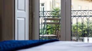 Ein Zimmer mit Bett, Blick auf einen Balkon mit Stuhl und ein Gebäude im Hintergrund.