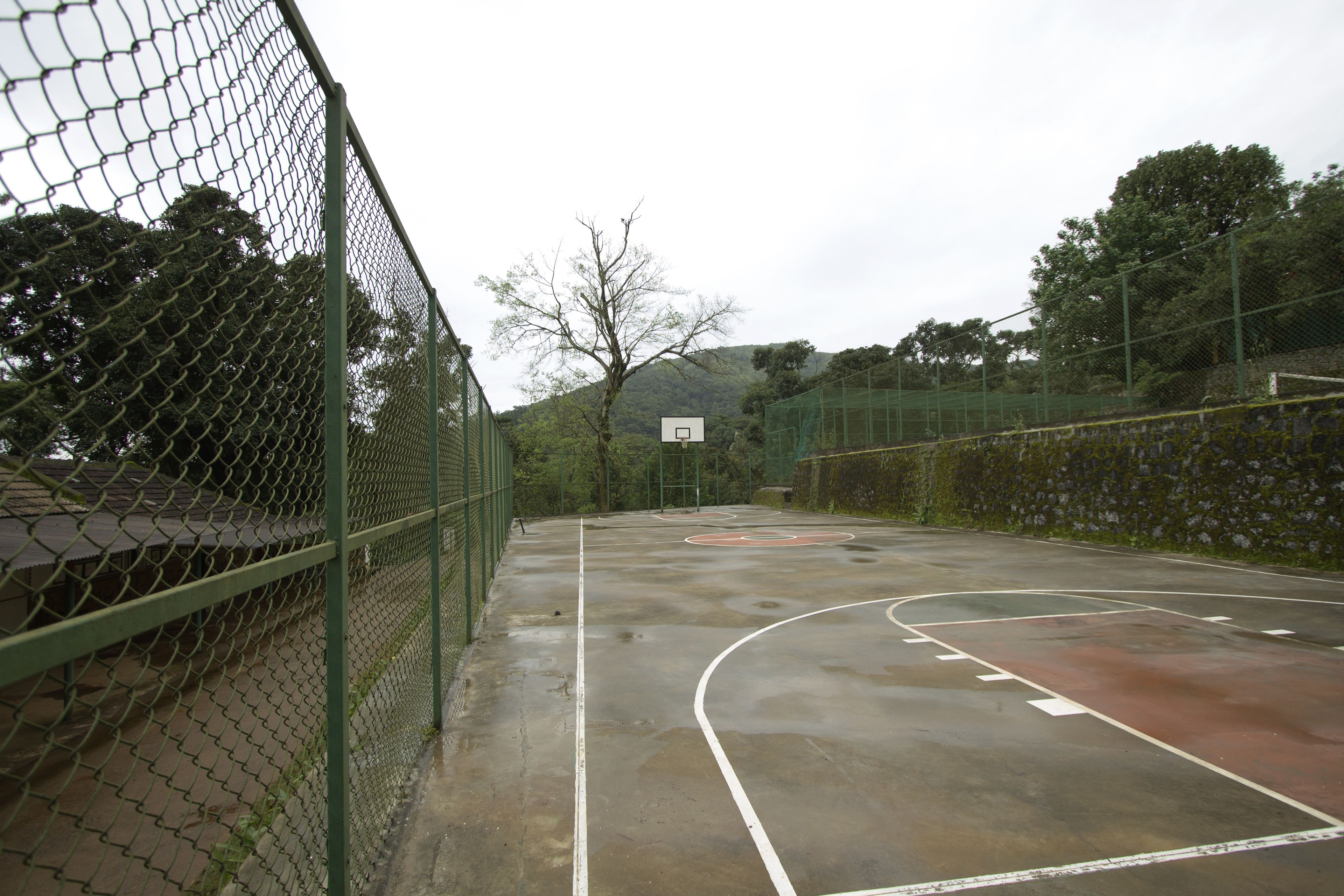 Una cancha de baloncesto al aire libre con una cerca de malla metálica, un aro de baloncesto y una red.