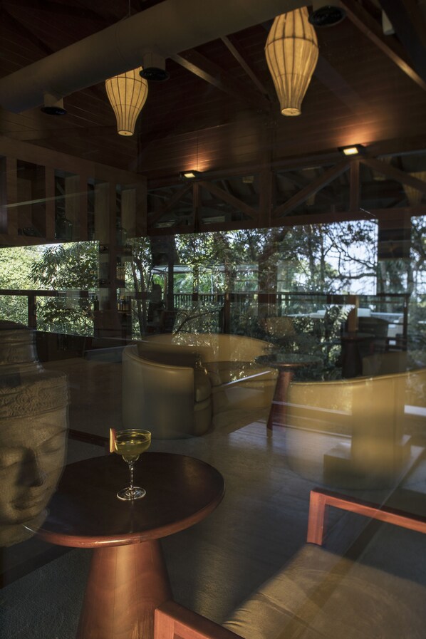 An indoor area with tables and chairs, a glass partition, and hanging light fixtures. - The Tamara Coorg (Madikeri)
