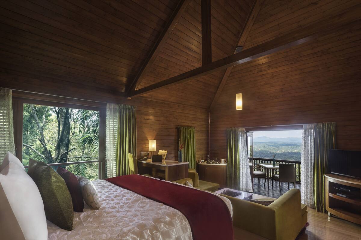 A spacious room with a large bed, a desk, a television, and a balcony with a view of the landscape.