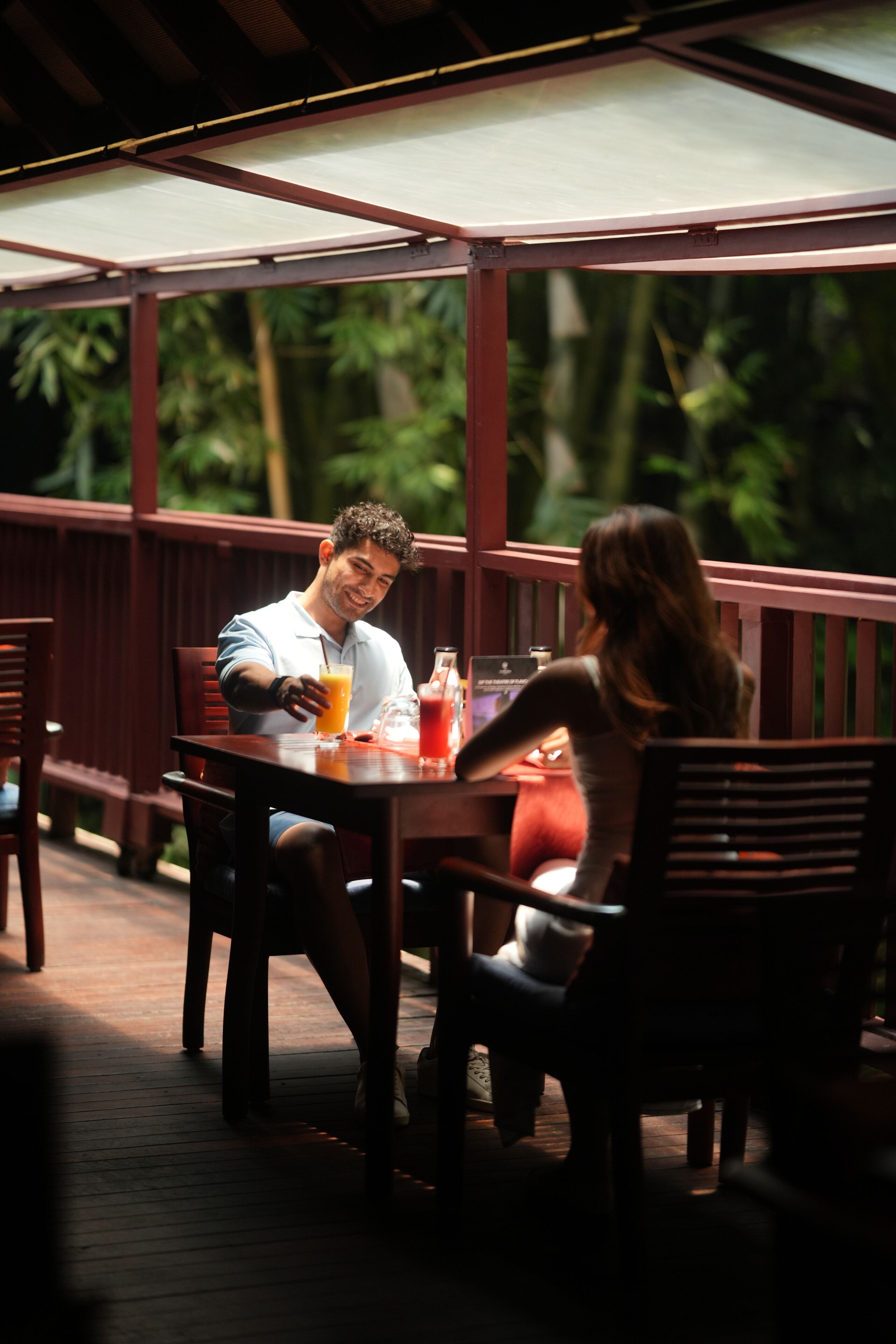 A covered outdoor dining area with wooden furniture and a table set for two.