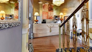A reception area with a wooden counter, a large mirror, and a staircase with ornate railings. - Hotel DaVinci (Marianske Lazne)