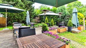 An outdoor patio area with wooden tables and chairs, green umbrellas, and potted plants. - Hotel DaVinci (Marianske Lazne)