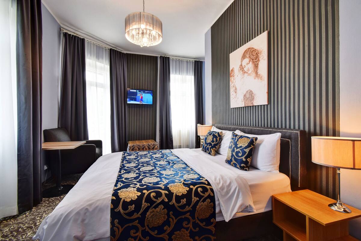 A hotel room with a large bed, a desk, a chair, a TV, and a painting on the wall.