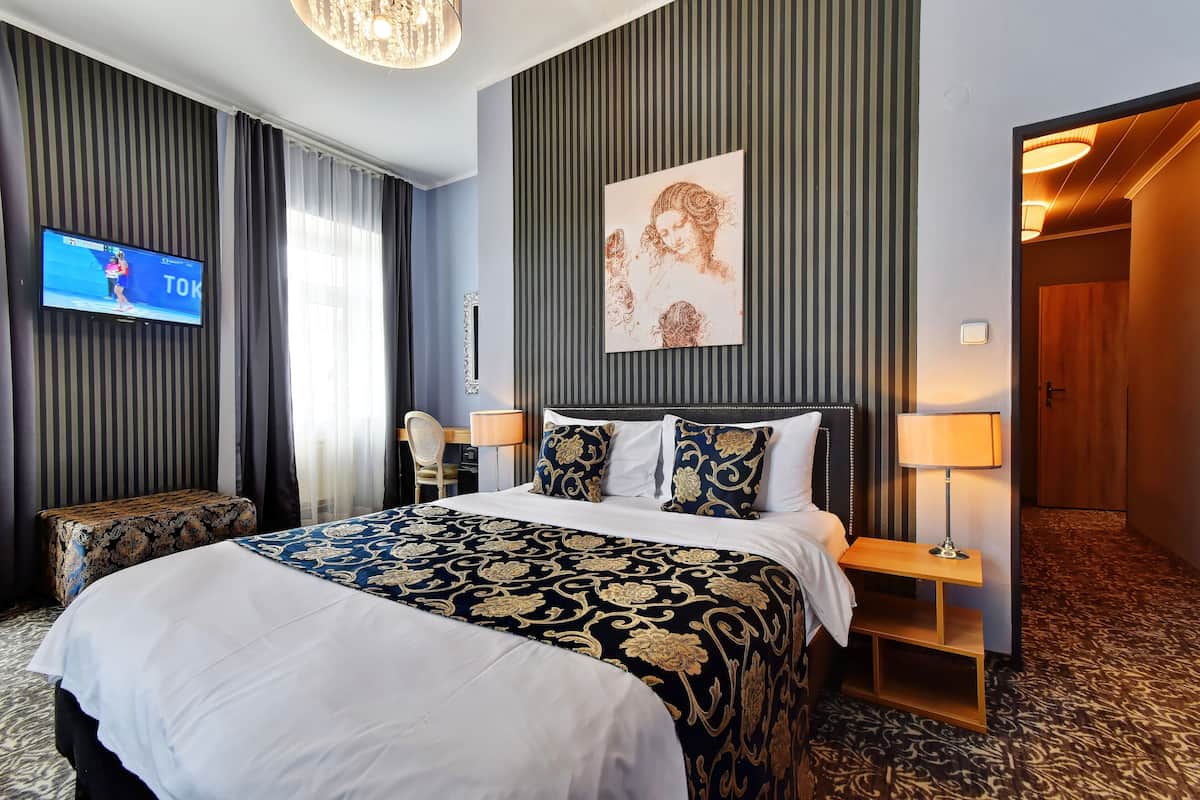 A hotel room with a large bed, a television, a painting on the wall, and a wooden nightstand.