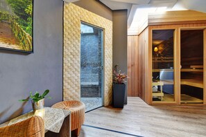 A modern interior with a glass door leading to a wooden deck, a wicker chair, a potted plant, and a wooden sauna. - Hotel DaVinci (Marianske Lazne)