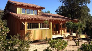 A wooden house with a tiled roof, large windows, and a porch. - WOODEN HOUSE IN THE BORDER OF THE OCEAN (Soulac-Sur-Mer)
