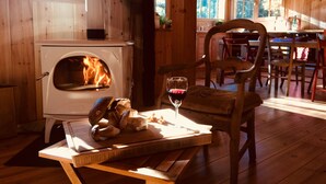 A cozy cabin interior with a wood-burning stove, a dining table with chairs, and a glass of red wine. - WOODEN HOUSE IN THE BORDER OF THE OCEAN (Soulac-Sur-Mer)