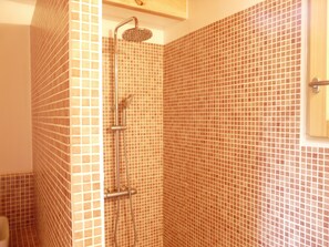 Un baño con zona de ducha, pared con azulejos y ducha.