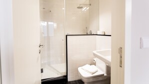 Un bagno moderno con doccia vetrata, un water bianco e un lavabo con piano in nero.