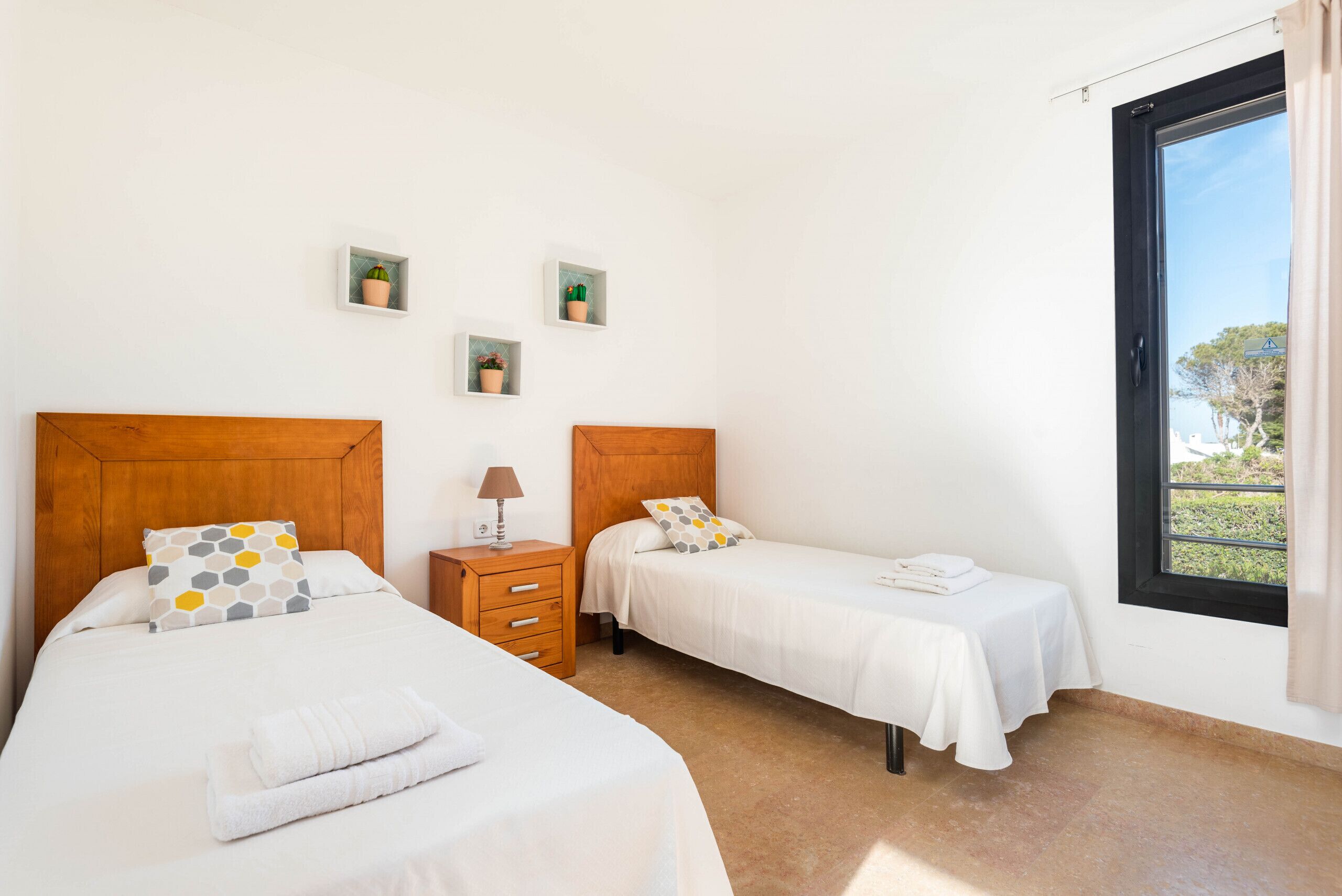 A bedroom with two beds, a nightstand with a lamp, and three small potted plants on the wall.