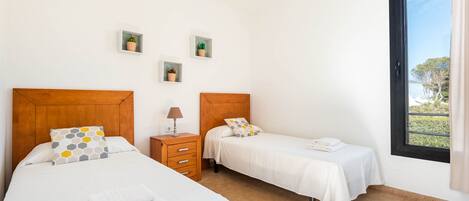A bedroom with two beds, a nightstand with a lamp, and three small potted plants on the wall.