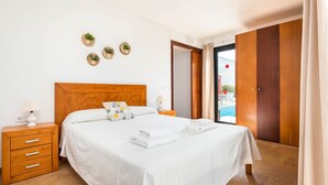 Ein ordentlich eingerichtetes Schlafzimmer mit einem hölzernen Kopfende, einem Nachttisch mit Lampe und Blick ins Freie.