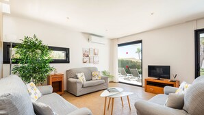 Ein modernes Wohnzimmer mit einem grauen Sofa, einem Couchtisch und einem Fernseher auf einem Holzboden. Ein großes Fenster bietet Blick auf Palmen und einen roten Ballon.