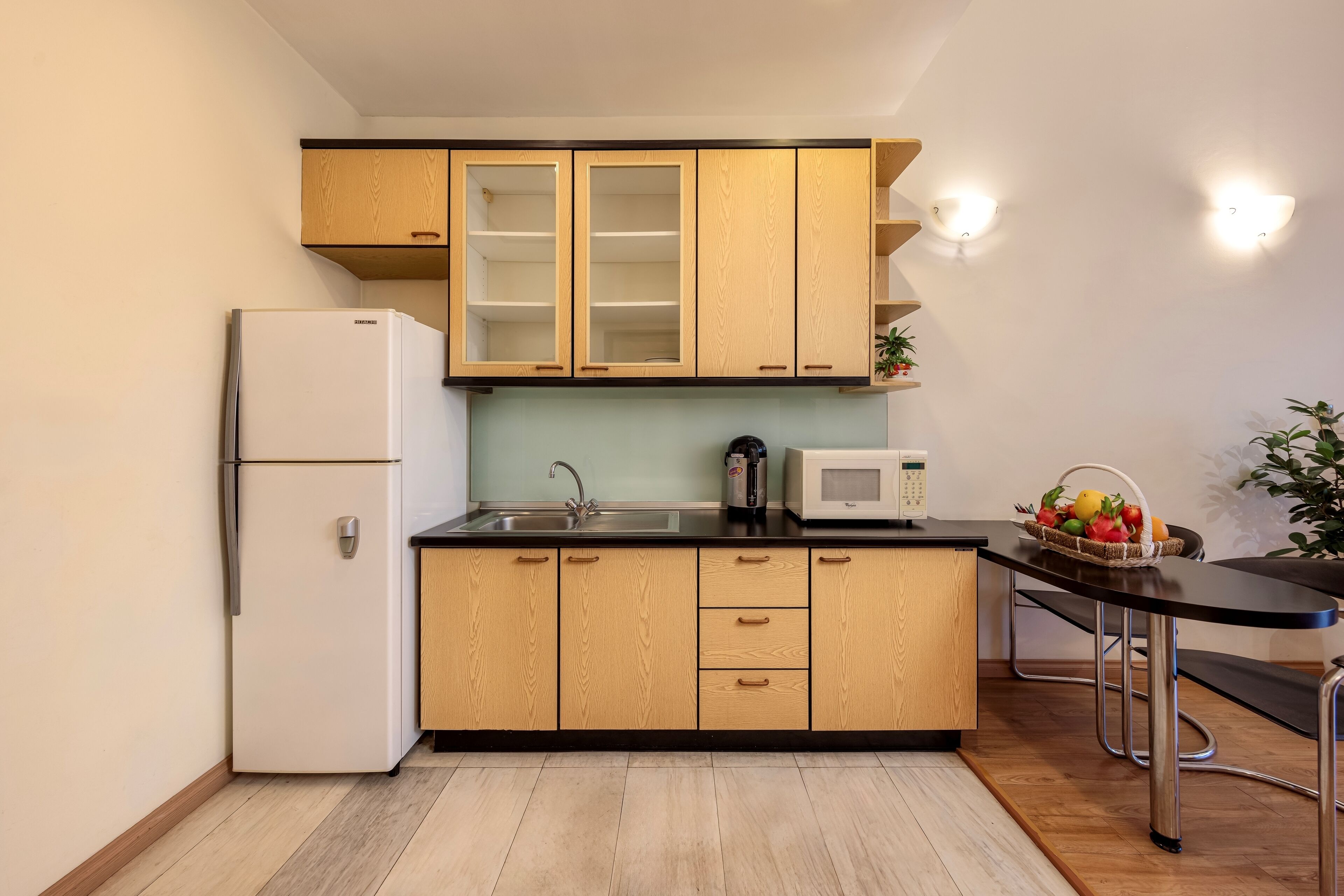 Una cocina compacta con armarios de madera, un refrigerador blanco, un microondas y un lavamanos.