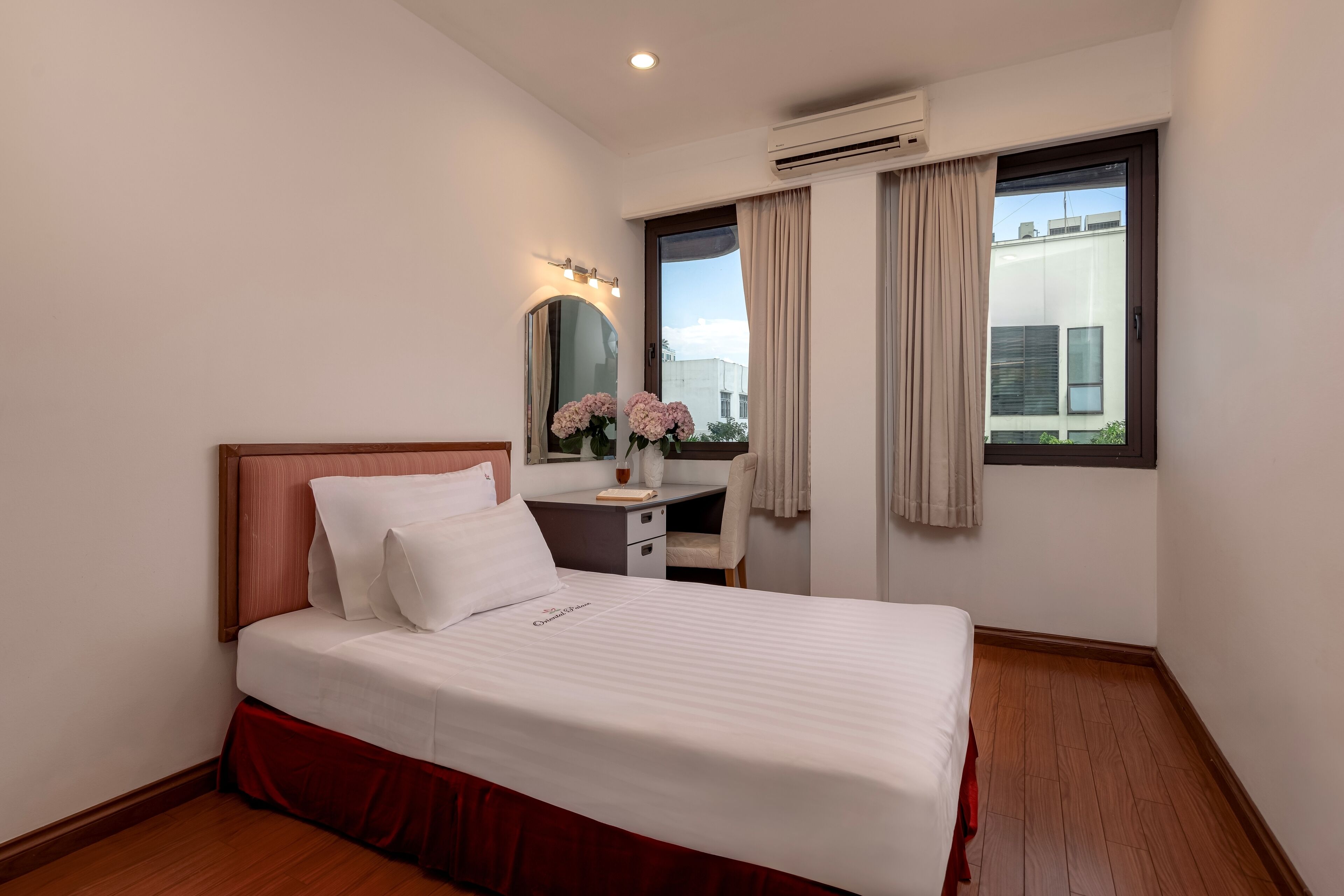 A neatly arranged hotel room with a bed, a desk, a mirror, and a window with curtains.