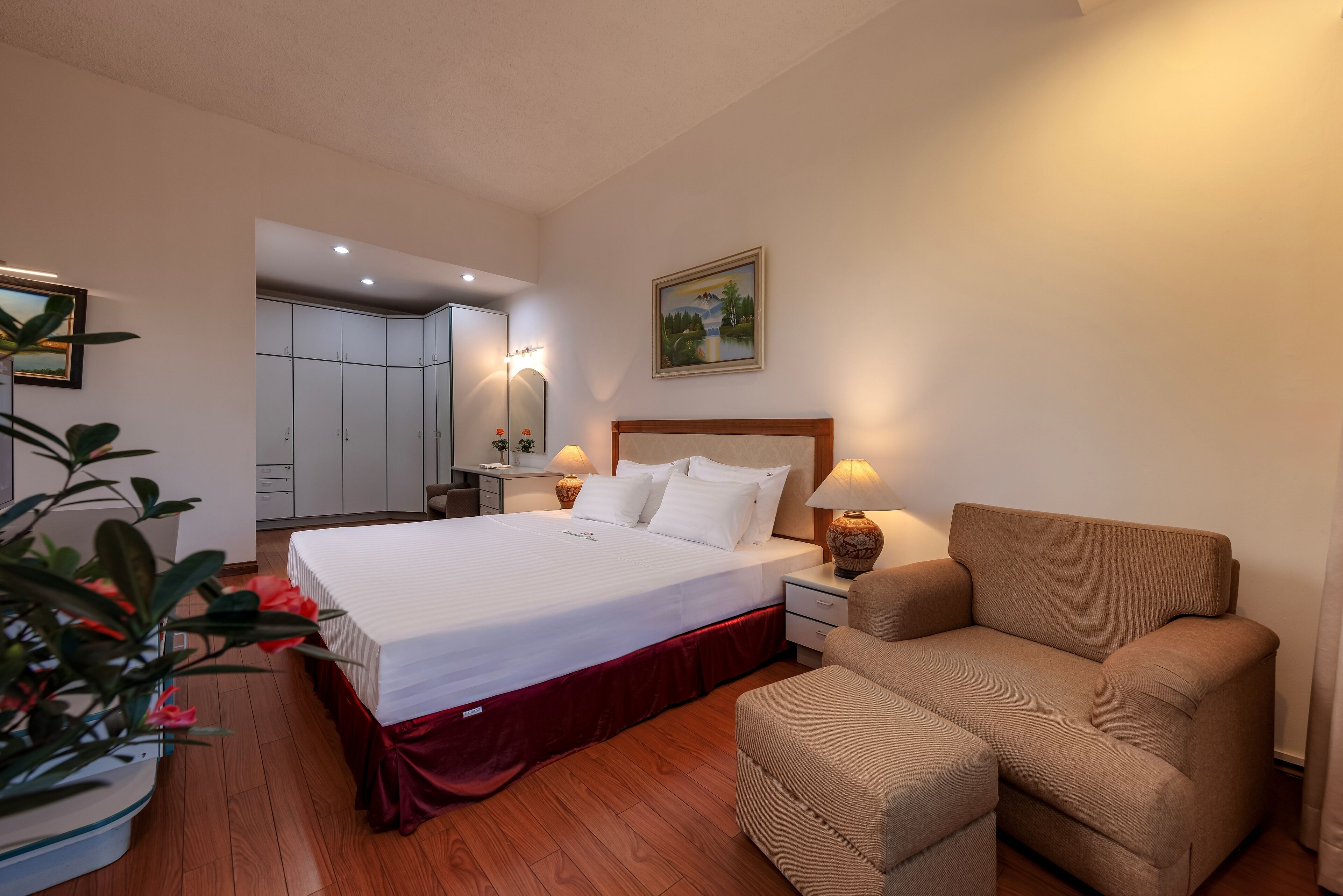 A hotel room with a large bed, a sofa, a nightstand with lamps, a mirror, and a painting on the wall.