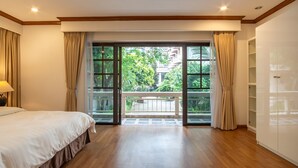 Een slaapkamer met een grote schuifglazen deur die leidt naar een balkon met uitzicht op groen en gebouwen.