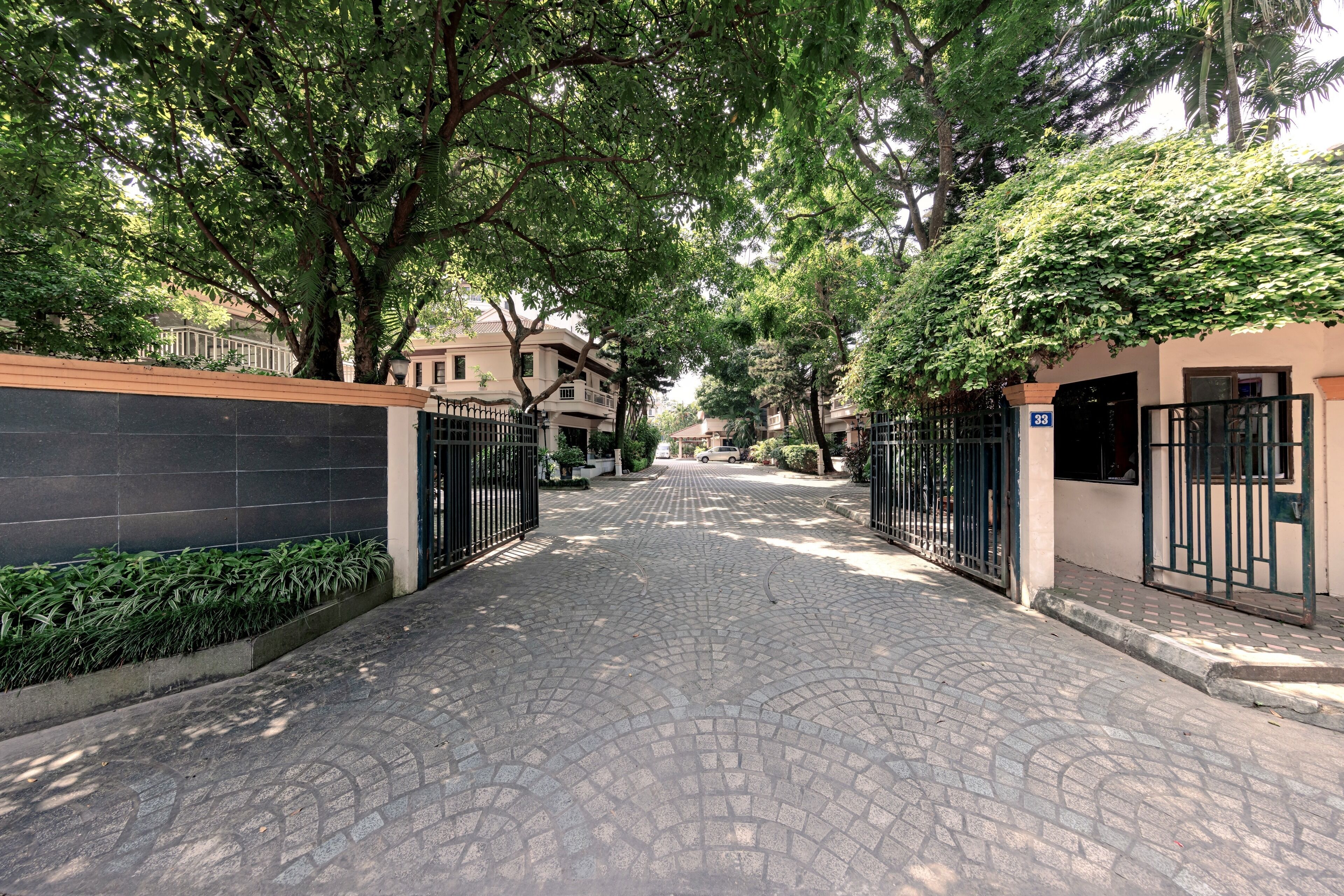 A paved pathway flanked by trees and gates leading to a building with a number sign.