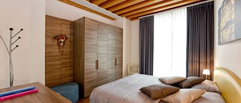 A bedroom with a wooden ceiling, a bed with multiple pillows, a nightstand, a wardrobe, and a window with curtains.