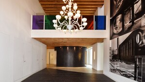 Ein geräumiger Flur mit einem modernen Kronleuchter, einer schwarzen, runden Säule und einem großformatigen Schwarz-Weiß-Wandgemälde an der rechten Wand.
