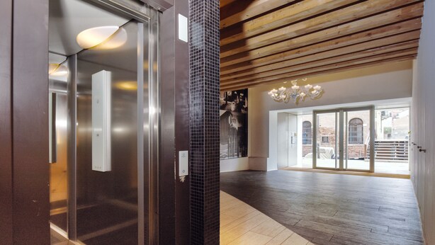 Ein modernes Interieur mit einem Glaselevator, einer Holzzieldecke und einem großen Fenster mit Außenblick.
