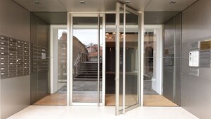 Ein Aufzug mit Glastüren, eine Wand aus Metall mit Briefschlitzen und eine Treppe, die zu einem Außenbereich führt.