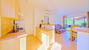 Una cocina moderna con una isla central, un comedor con mesa y sillas, y vistas a un jardín exuberante a través de amplios ventanales.