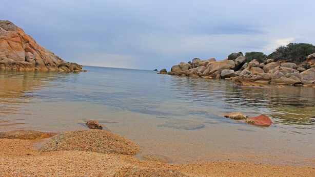 Un paisaje costero con agua cristalina, playa de guijarros y grandes rocas.