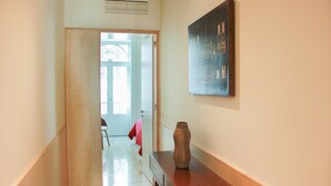 Un pasillo con piso de madera, un banco de madera con un florero y un cuadro en la pared.