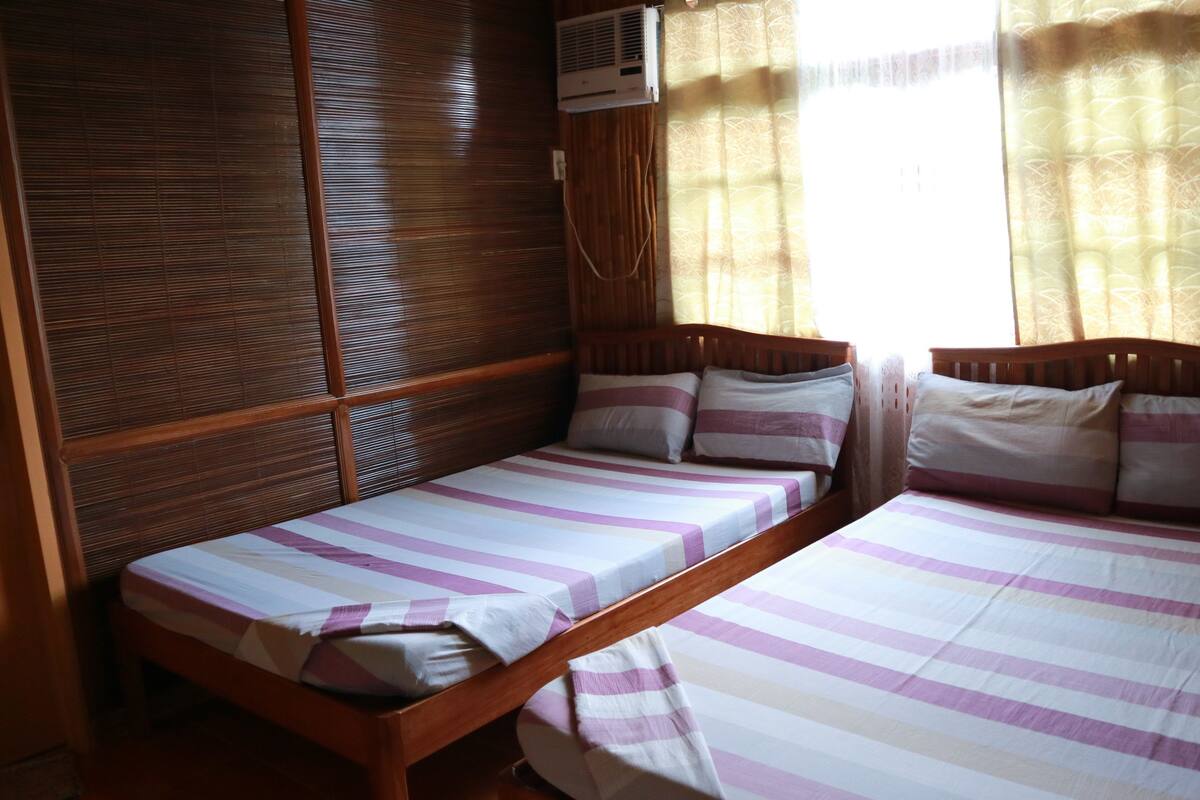 A room with two single beds, wooden headboards, and a window with curtains.