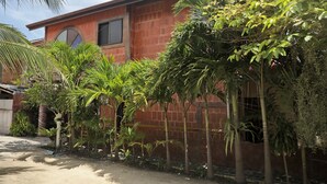 A red brick house with a small window and a door, surrounded by lush greenery including palm trees and other plants. - Villa Kamala Beach (Kamala)
