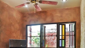 A living room with a ceiling fan, a television on a wooden stand, a sofa, and a window with colorful panes. - Villa Kamala Beach (Kamala)